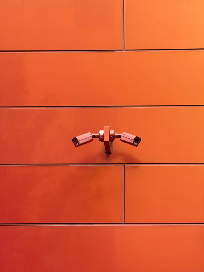 Two CCTV cameras mounted on a vibrant orange wall, showcasing modern surveillance.